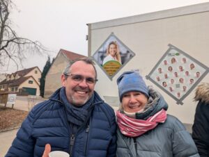 Der amtierende Bürgermeister Stefan Kumpf (CSU) und Herausforderin Maren Polke-Lanzl (COMPAKT – Liste Karlskron) lächeln gemeinsam in die Kamera. Sie stehen vor einem Kampagnenfahrzeug, das mit Porträtfotos der Wahlliste beklebt ist.