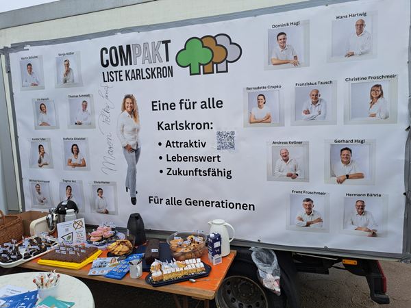 Ein reich gedeckter Tisch mit Kuchen, Gebäck und Flyern vor der Werbeplane der COMPAKT-Liste Karlskron.